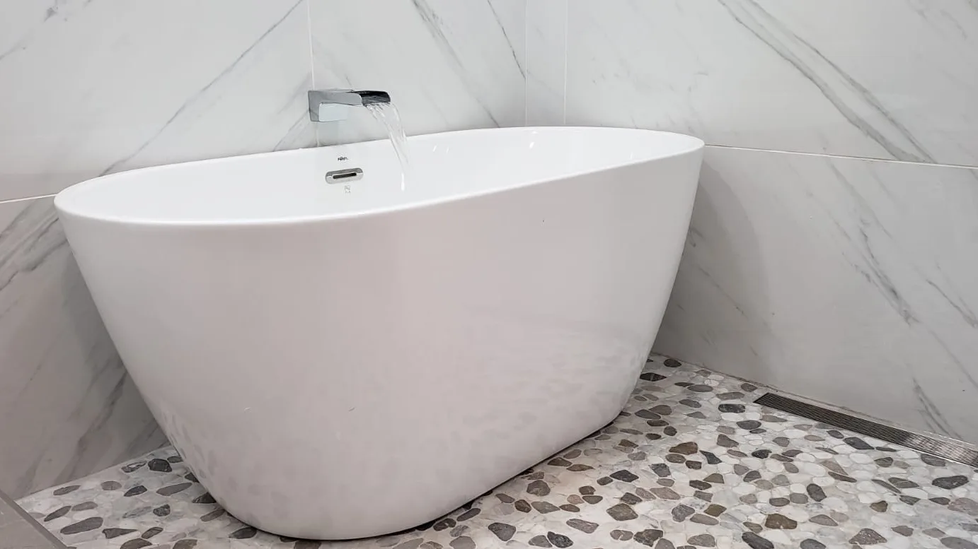 Freestanding soaking tub with wall-mounted chrome filler and pebble floor