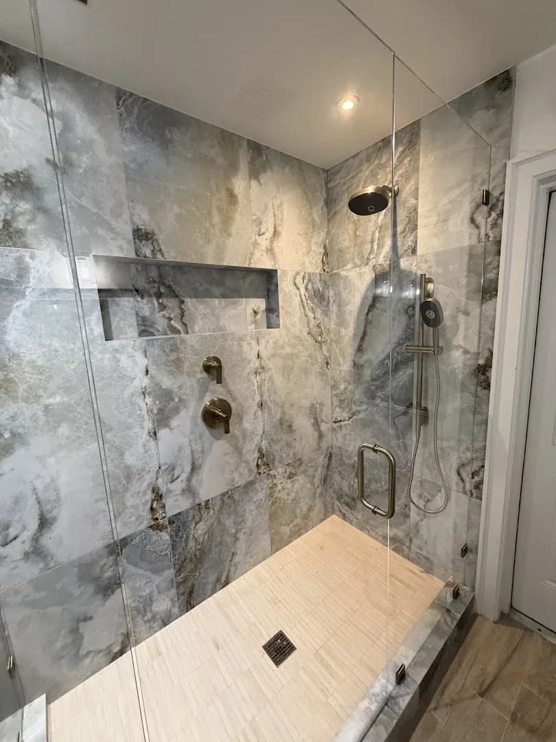 Walk-in shower with marble-look tile, rainfall head, and brushed bronze fixtures